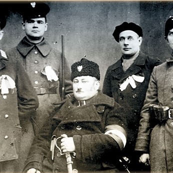 Czarno białe zdjęcie pięciu mężczyzn z bronią i wstążkami powstańczymi.