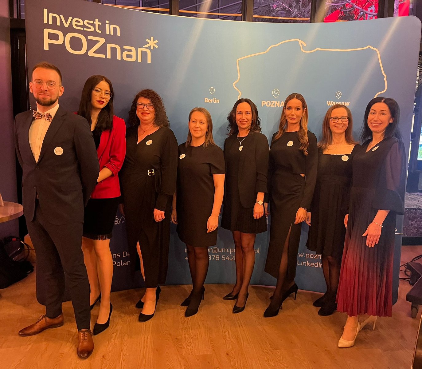 The photo shows Investor Relations Department team in evening clothes. In the background is a blue wall with the Invest in Poznań logo. - grafika artykułu