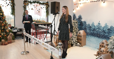 The photo shows Katja Lozina, director of the Investor Relations Department, speaking. In the background is a festive wall with company logos, including SOFTSWISS.